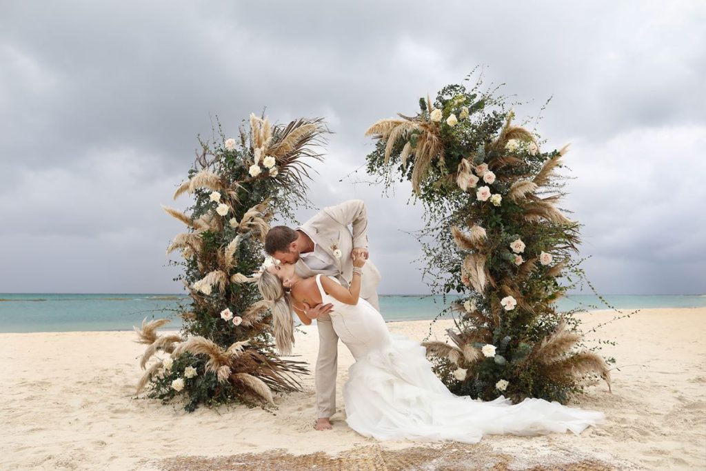 a just married couple kissing in front of their wedding arch at fairmont mayakoba