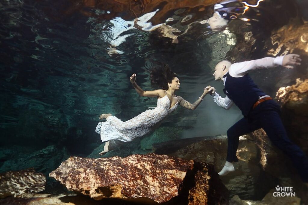 a just married couple during a trash the dress photo session in a cenote in mexico