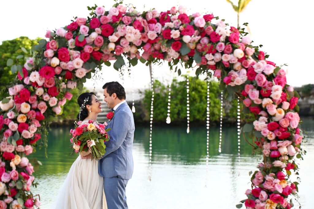 Married couple posting with a flower arch and the beach in the background